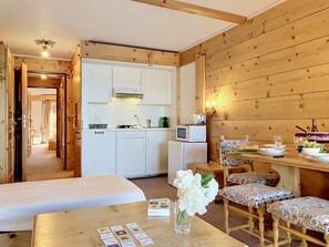 Een compacte kamer met een kitchenette, een eethoek met een tafel en stoelen, en een bed.