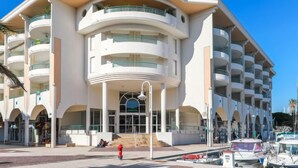 A modern hotel with multiple balconies, a central entrance with a glass facade, and a parking area with boats. - Apartment L'Open by Interhome (Fréjus)
