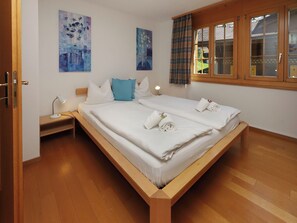 A double bed with white linens, two bedside tables with lamps, and two paintings on the wall. - Chalet Nagano by Interhome (Grindelwald)