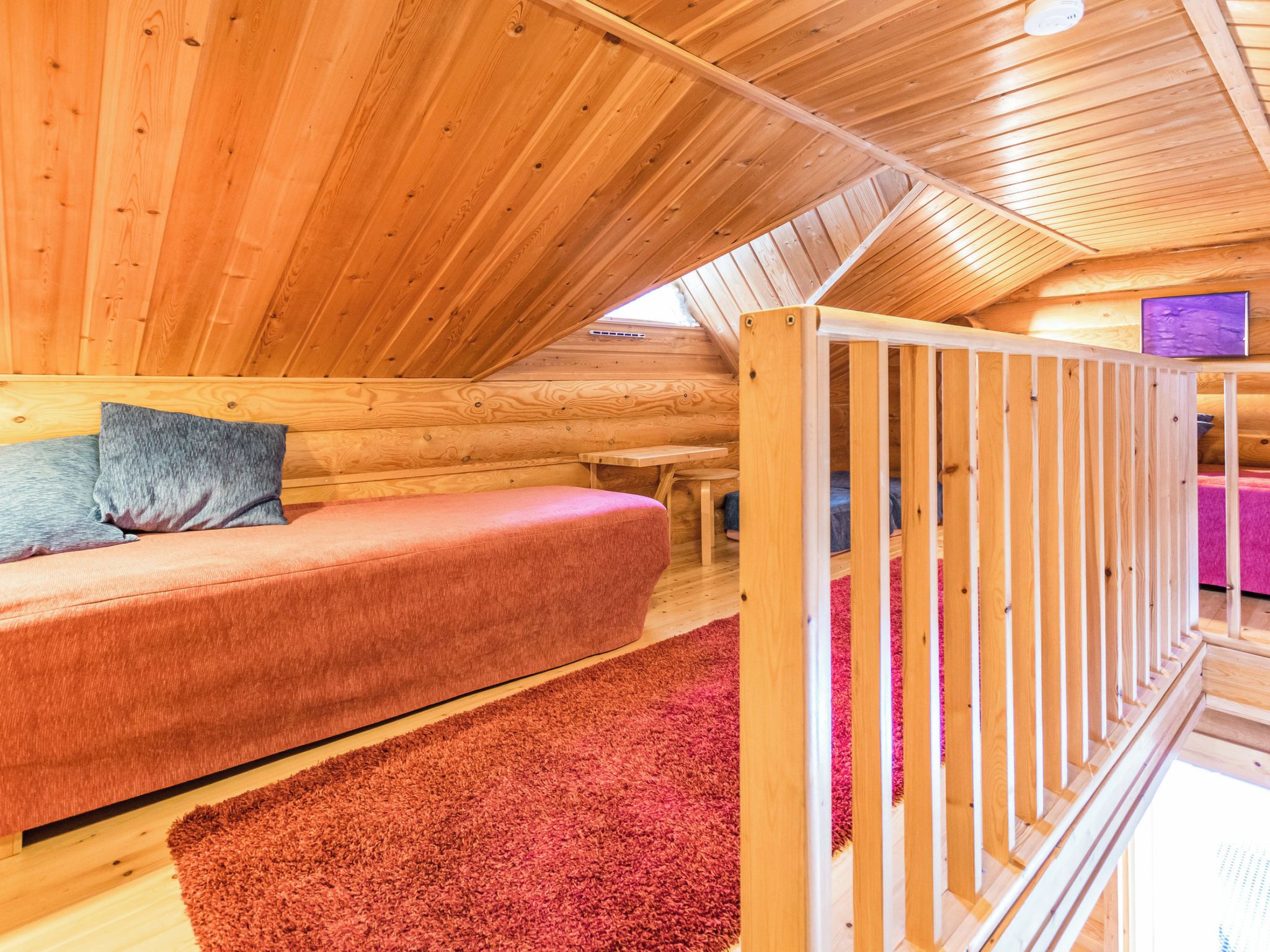 A cozy wooden cabin interior with a sofa, a small table, and a red carpet.
