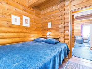 Une chambre dans un chalet en rondins, avec un lit, des tableaux encadrés au mur et une fenêtre avec des rideaux.