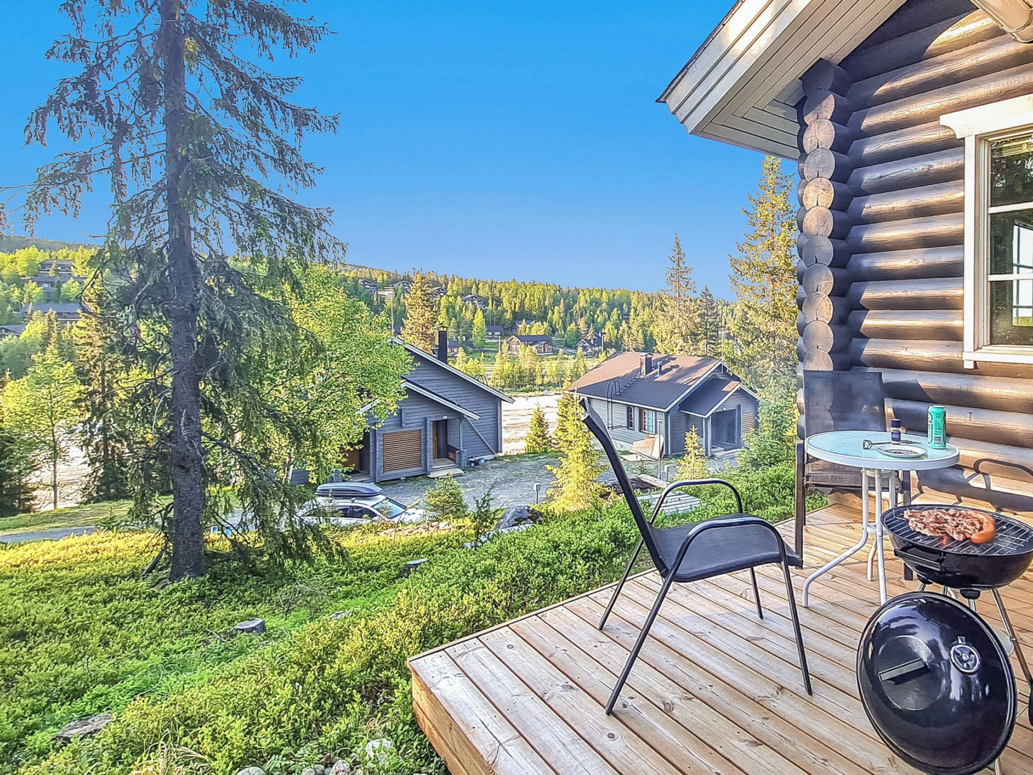 A wooden deck with a grill and outdoor seating, overlooking a residential area with houses and trees.