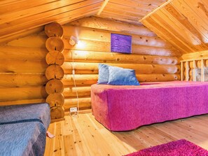 A cozy log cabin room with a bed, a blue pillow, and a purple wall hanging.