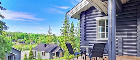 Eine Blockhütte mit einer Terrasse, Sitzgelegenheiten im Freien und Blick auf eine bewaldete Landschaft.