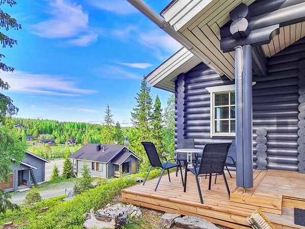 A log cabin with a deck, outdoor seating, and a view of a forested area.