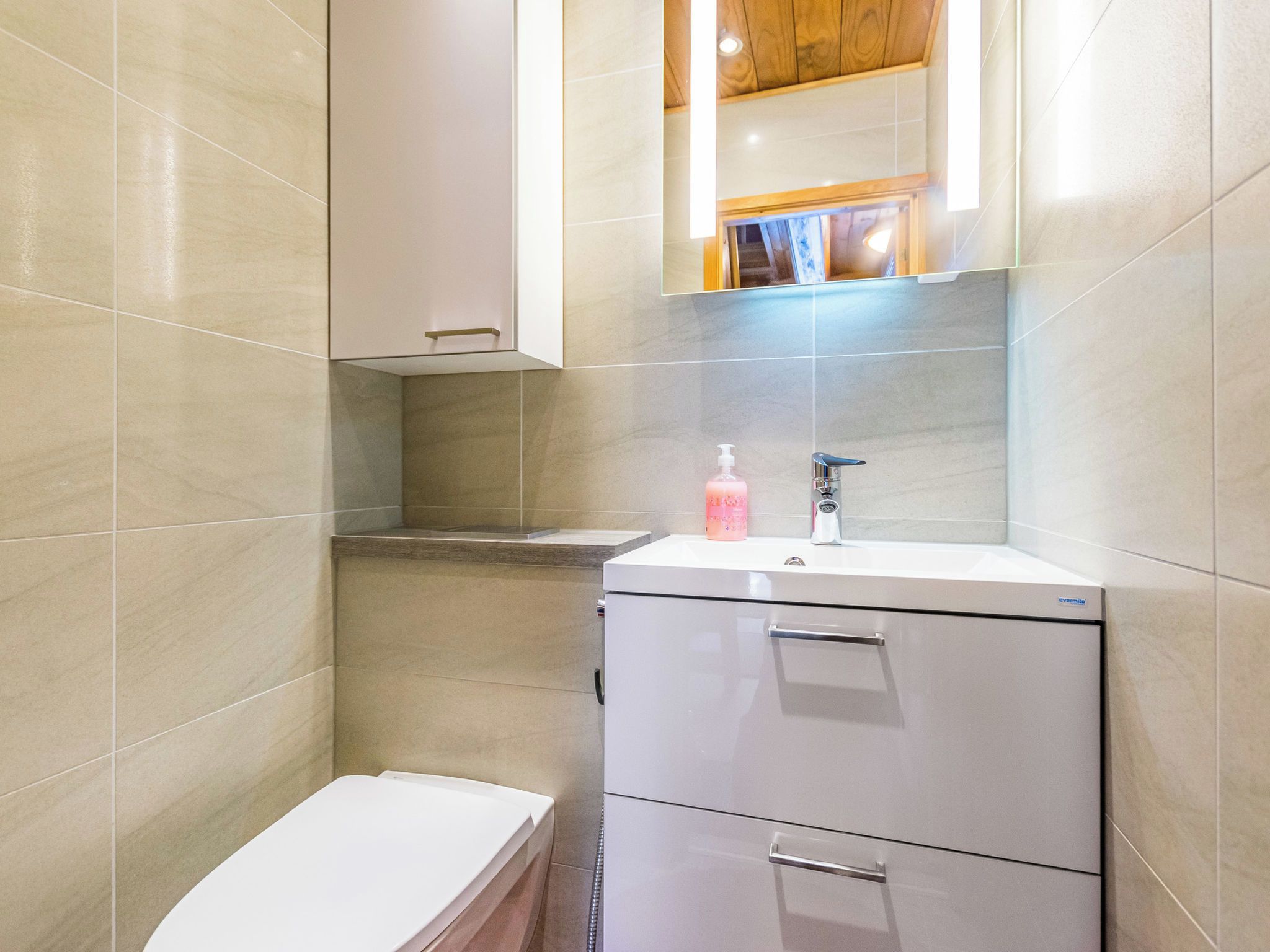 A modern bathroom with a toilet, a sink with a soap dispenser, and a mirror above the sink.