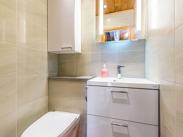 A modern bathroom with a toilet, a sink with a soap dispenser, and a mirror above the sink.