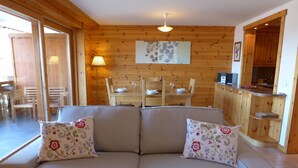A cozy living room with a sofa, a dining table, and wooden walls. - Rhodonite 33 by Interhome (Villars)