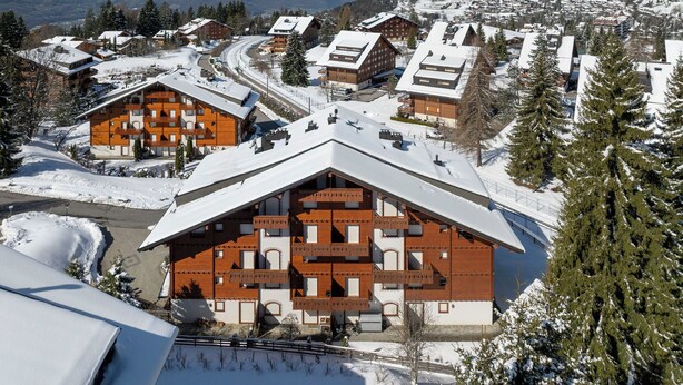 A snow-covered mountain town with wooden buildings, a ski slope, and a view of snow-capped mountains. - Rhodonite 33 by Interhome (Villars)