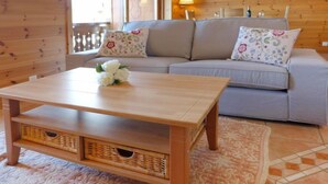 A wooden coffee table with wicker baskets, a grey sofa with floral cushions, and a patterned rug in a cozy room with wooden walls. - Rhodonite 33 by Interhome (Villars)