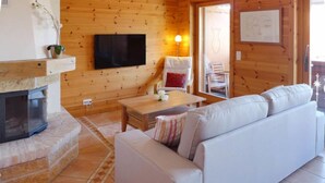 A cozy living room with a fireplace, a sofa, a TV mounted on the wall, and a wooden interior. - Rhodonite 33 by Interhome (Villars)