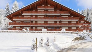 A multi-story wooden building with balconies, surrounded by snow-covered trees. - Rhodonite 33 by Interhome (Villars)