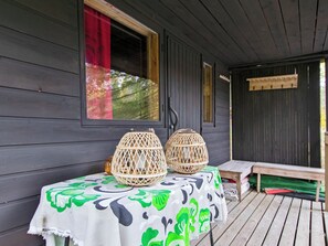 A wooden porch with a table covered by a green and white patterned tablecloth, two wicker lanterns, and a bench. - Koskimökki, vaikon loma 3 by Interhome (Kaavi)
