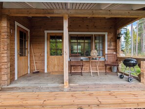 A wooden cabin with a porch, a dining table, chairs, a grill, and a window overlooking a forest. - Koskimökki, vaikon loma 3 by Interhome (Kaavi)