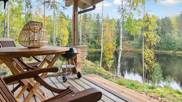 A wooden deck with a table and chairs, overlooking a lake surrounded by trees. - Koskimökki, vaikon loma 3 by Interhome (Kaavi)