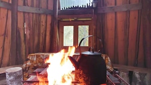 A rustic cabin interior with a wood-burning stove, a kettle, and a window with a view of trees. - Koskimökki, vaikon loma 3 by Interhome (Kaavi)