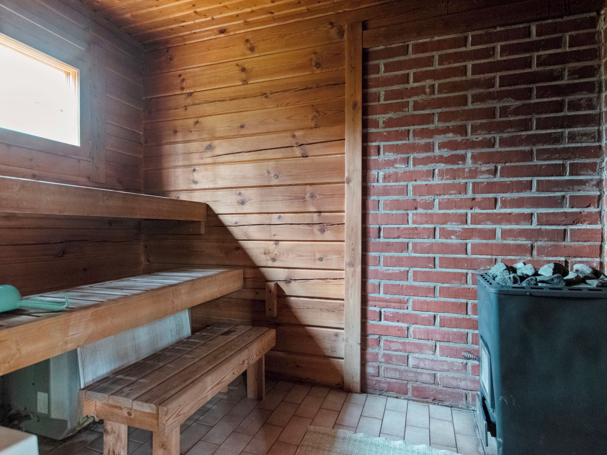 Interno di una casetta di legno con una panca, un muro in mattoni e una finestra.
