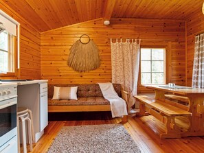 Interior acogedor de una cabaña con detalles de madera, un sofá, una mesa de comedor y una zona de cocina.