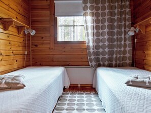 A cabin with two beds, wooden walls, a window, and a curtain with a polka dot pattern.