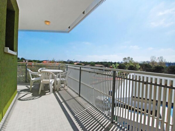 A balcony with a white table and chairs, a metal railing, and a view of buildings and trees.