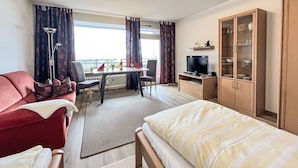 A hotel room with a bed, a desk with a TV, a wardrobe, a dining table with chairs, and a view of the outdoors. - Braubach (B715) by Interhome (Lahnstein (Koblenz))