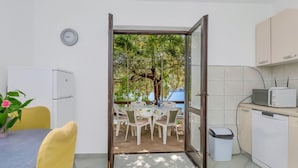 Une cuisine compacte avec un coin repas, une vue sur la verdure et une horloge au mur.