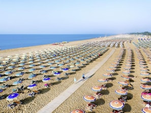 Une plage bordée de rangées de parasols et de chaises, un ciel dégagé et l’océan en toile de fond.