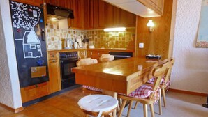 A kitchen with wooden cabinets, a tiled backsplash, a central island, and a dining area with chairs. - Les Aiguilles d'Argent 10 by Interhome (Villars)