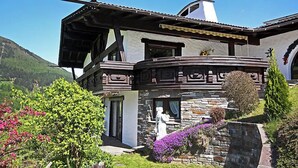 Una casa de dos plantas con fachada de piedra, un balcón y un jardín con flores y arbustos.