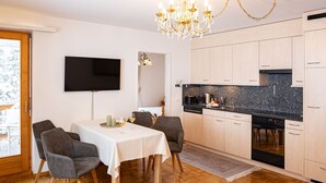 A modern kitchen with a black granite countertop, wooden cabinets, and a built-in oven. There is a dining area with a table and chairs, and a chandelier above.