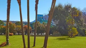 A well-maintained grassy area with palm trees and a modern building in the background. - Residenza Lido Appartment 008 by Interhome (Locarno)