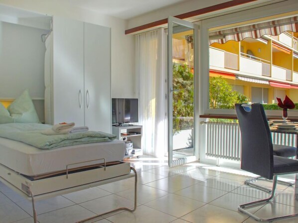 A modern hotel room with a bed, a TV, and a balcony with a dining area.