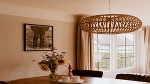 Un comedor con una mesa de madera, sillas, un jarrón con flores, una vela y un cuadro en la pared.