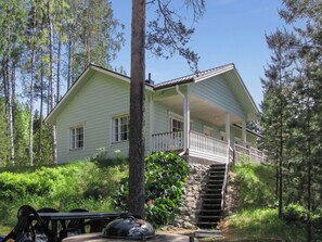 Une maison à deux étages avec un porche, entourée d’arbres et dotée d’un escalier en pierre menant à l’entrée.