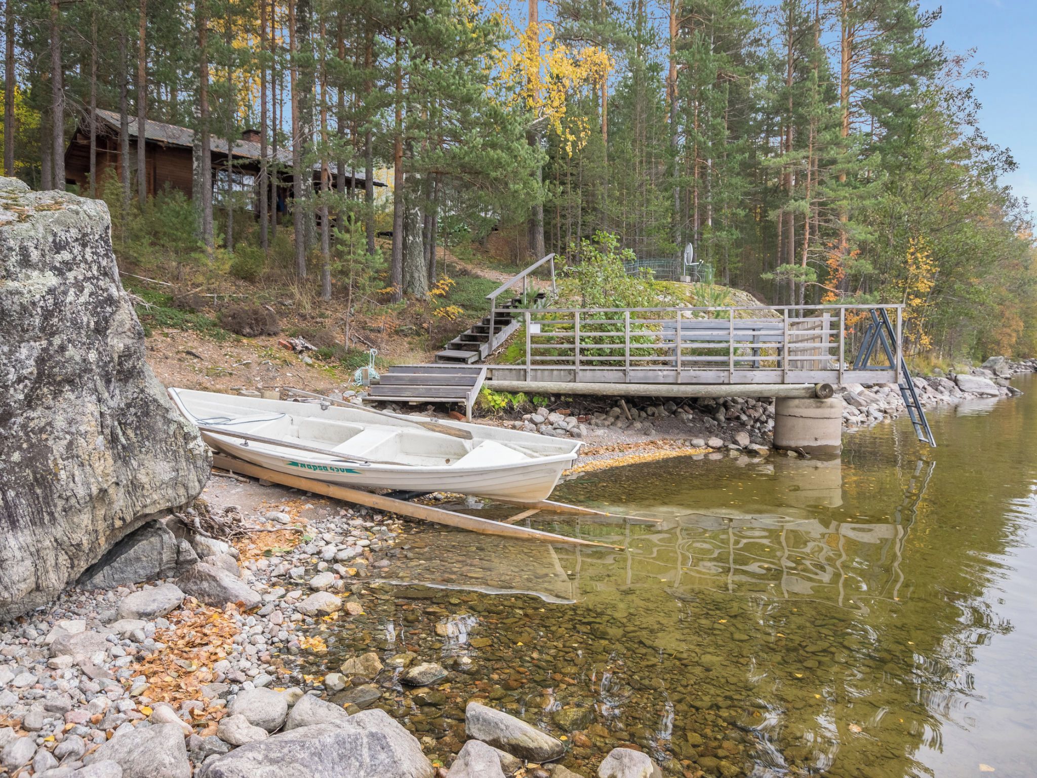 A wooden boat docked at a rocky shore with a bridge leading to a cabin in a forested area.