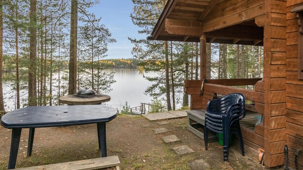 Una baita di legno con una veranda che si affaccia su un lago, circondata da alberi.