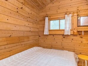 A wooden cabin room with a bed, a window with curtains, and a small table. - Päivärinne by Interhome (Punkaharju)