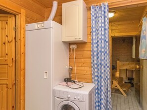 Een kleine wasruimte met een wasmachine en droger, een wit kastje boven de droger, en een douchegordijn met ruitpatroon.