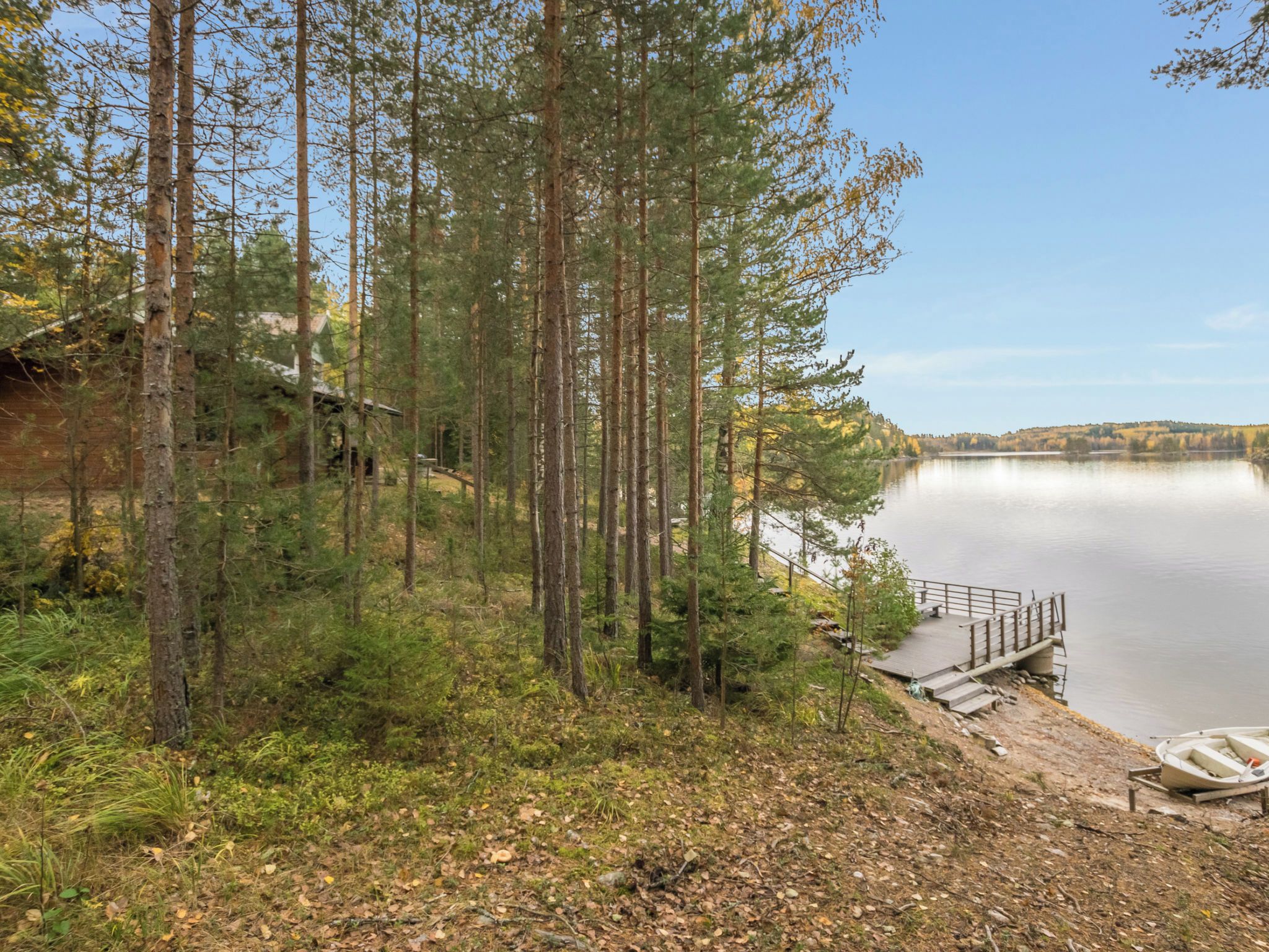 A lakeside cabin with a dock extending into the water, surrounded by tall trees and a clear sky.