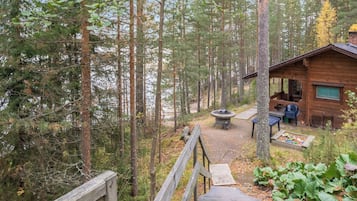 Puinen terassi, joka johtaa mökille, jossa on nuotiopaikka ja ulkotila istumiseen.