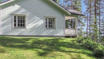 A single-story house with a porch, surrounded by a grassy yard and tall pine trees.