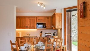 A cozy kitchen with wooden cabinets, a dining table set for four, and a red sofa in the foreground. - Les Cimes Blanches 102 A by Interhome (Nendaz)