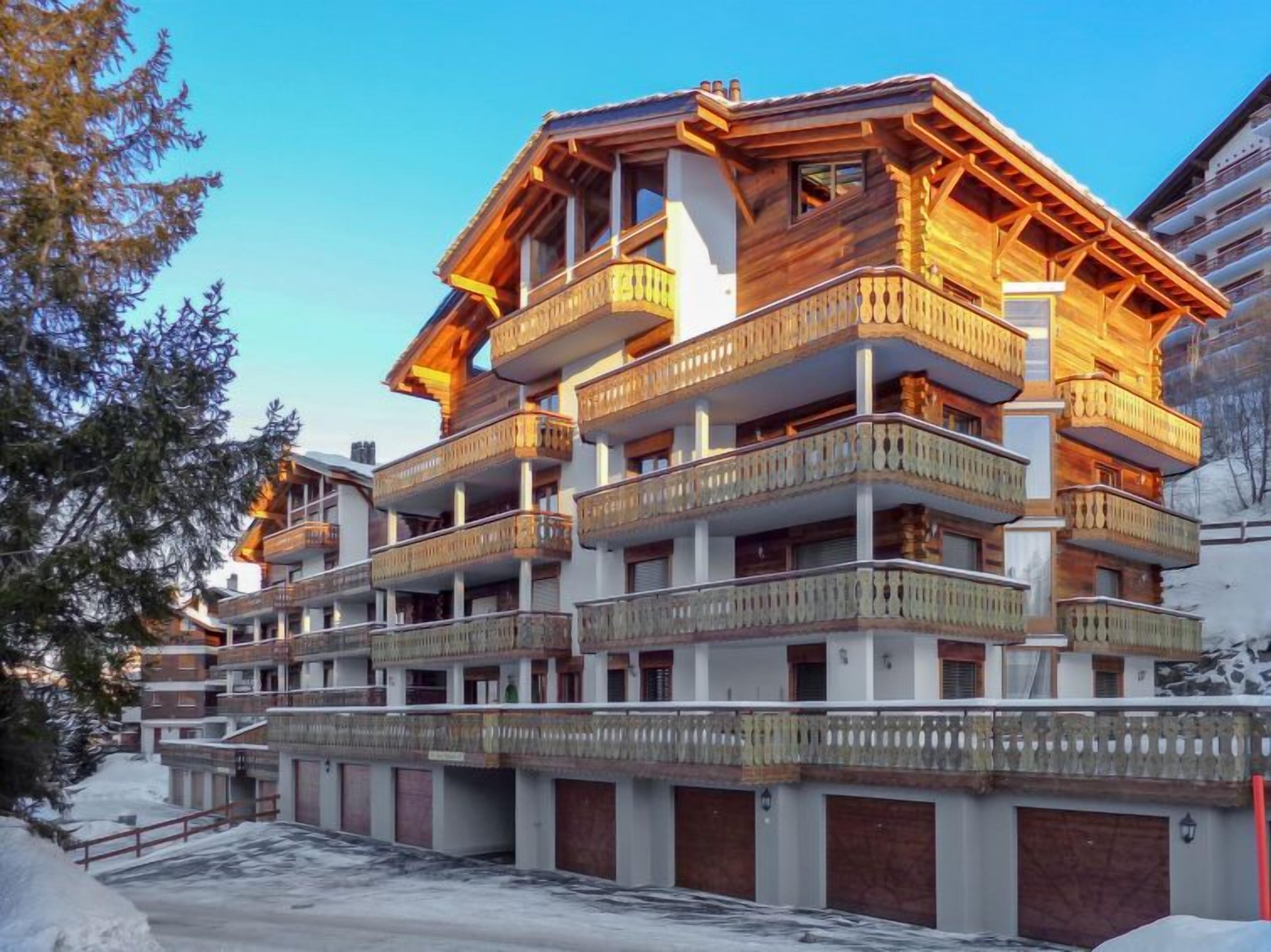 Um hotel de vários andares com varandas de madeira e uma pista de esqui ao fundo.