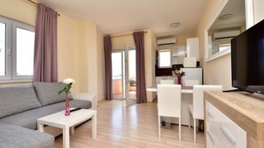 En moderne, lys stue med en grå sofa, et lille hvidt bord med en vase blomster, og et fjernsyn på et træskab.