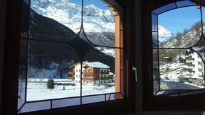 A room with large windows offering views of snow-covered mountains and a building with a wooden facade. - Theresli by Interhome (Saas-Almagell)