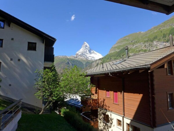 A chalet with a wooden exterior and a balcony, set against a backdrop of a mountain and a clear sky.