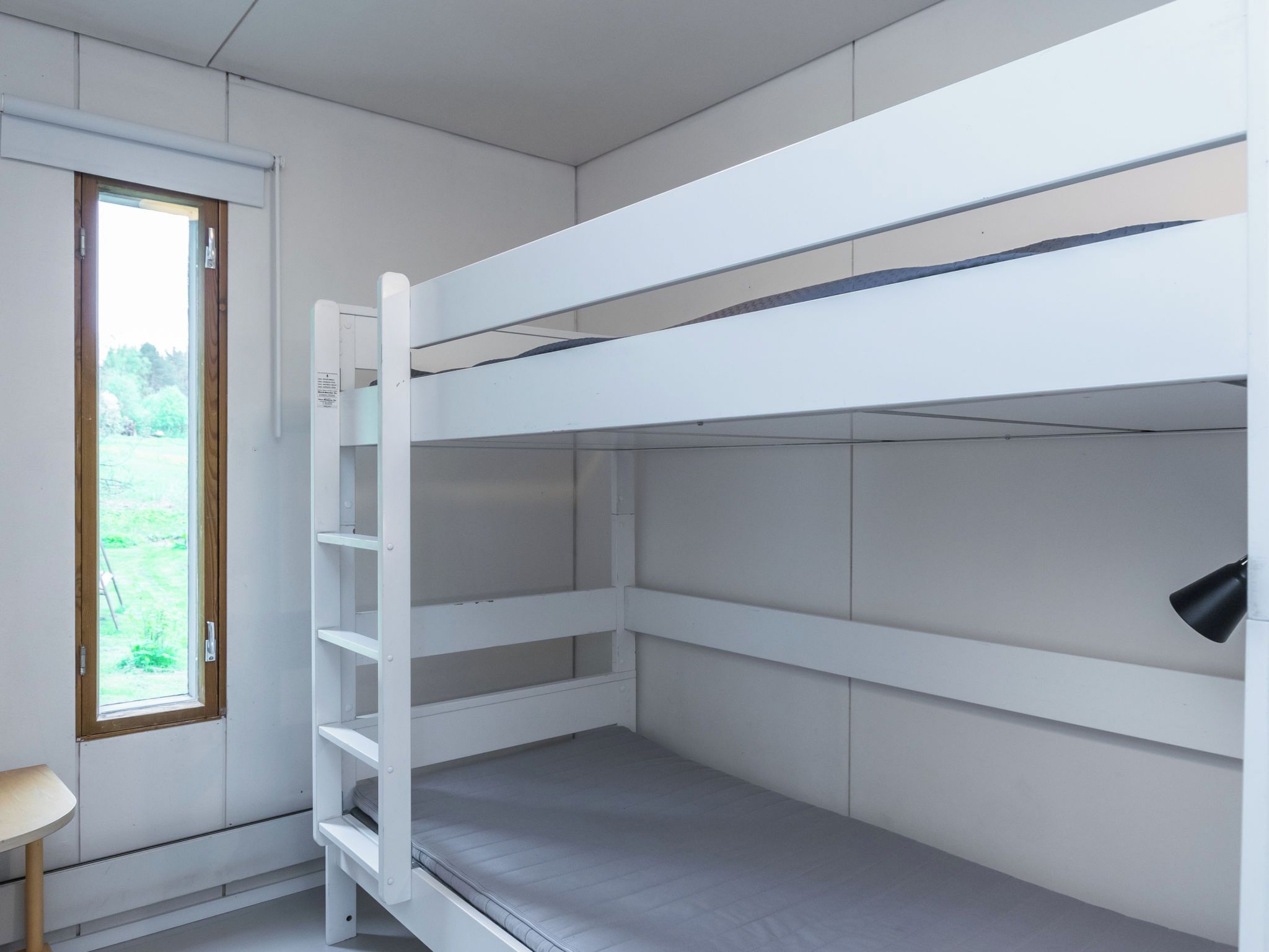 Una cama litera con ventana, una mesita pequeña y una lámpara fijada a la pared.