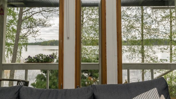 Une pièce avec vue sur un lac, une terrasse en bois et un canapé gris agrémenté d’un coussin à rayures.