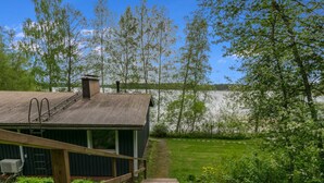 Un escalier en bois mène à un chalet rustique doté d’un toit en métal, entouré d’une végétation luxuriante et bordé par un lac.