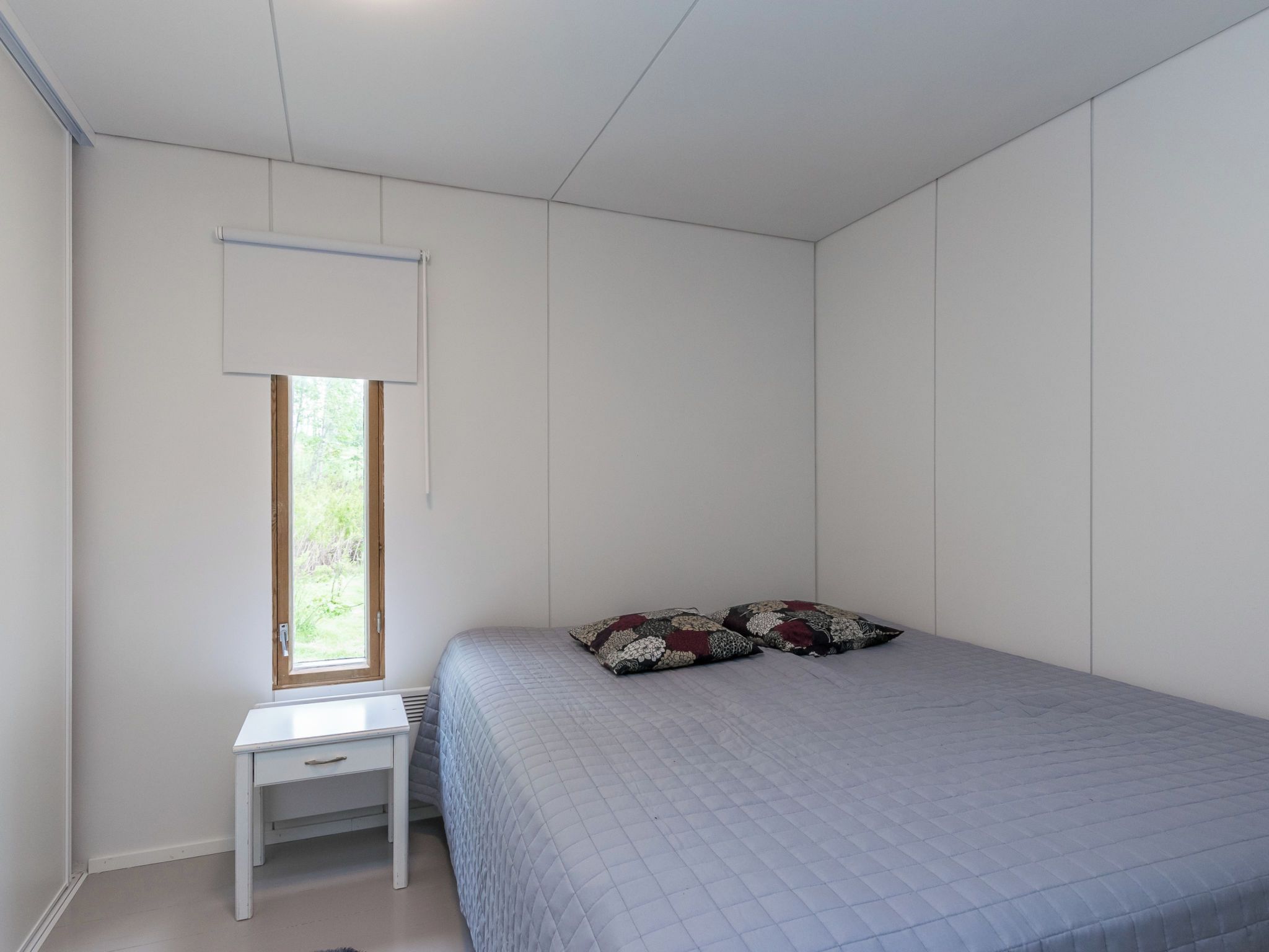 A bedroom with a single bed, a small bedside table, and a window with a white blind.